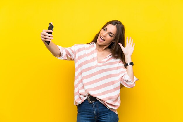 Молодая женщина изолированная на желтом цвете делая selfie