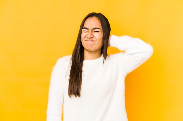 Young woman isolated on a yellow space suffering neck pain due to sedentary lifestyle.