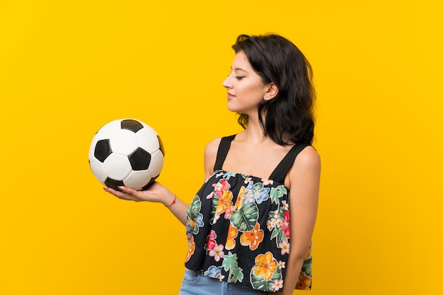 Young woman over isolated yellow wall holding a soccer ball