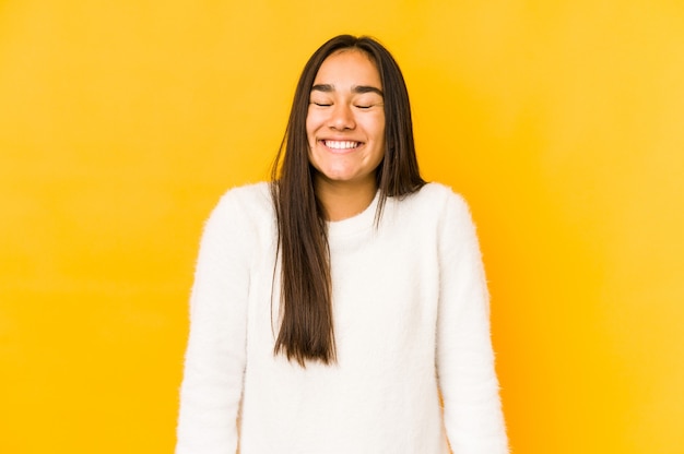 Young woman isolated on a yellow wall laughs and closes eyes, feels relaxed and happy