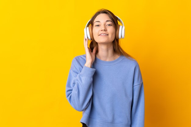 Young woman isolated on yellow wall listening music