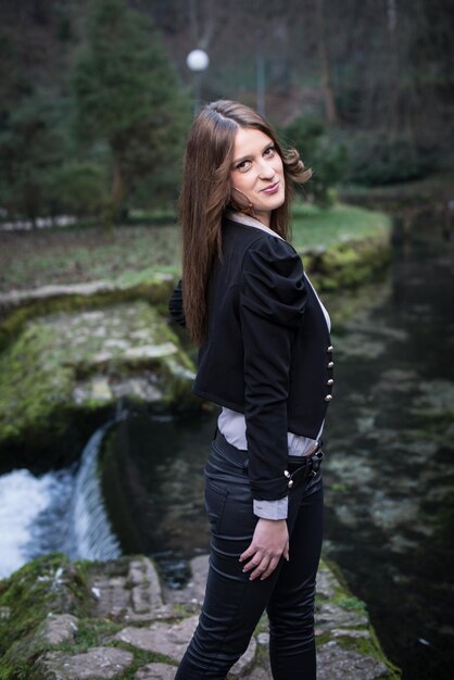 young woman in jacket looking behind her shoulder and smiling at the lake