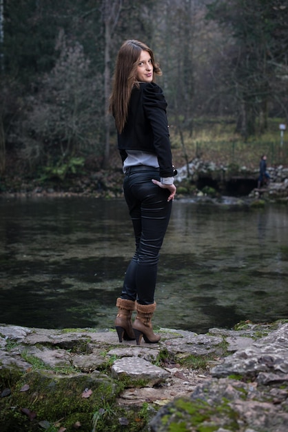 young woman in jacket looking behind her shoulder and smiling at the lake