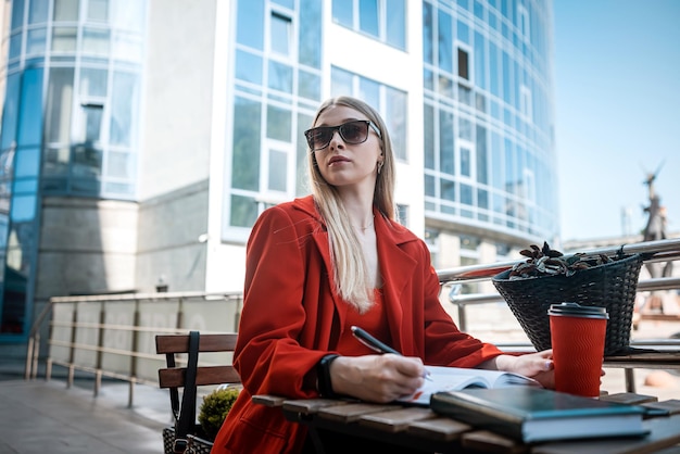 A young woman in a jacket works on a netbook in a cafe on the terrace Autumn morning Street style