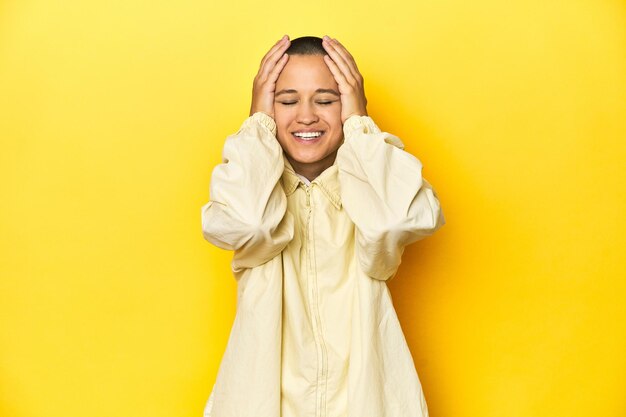 Photo young woman in jacket yellow studio backdrop laughs joyfully keeping hands on head happiness concept