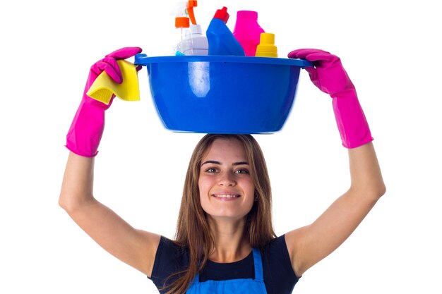 Young woman in jeans and apron with pink gloves holding cleaning things in blue washbowl