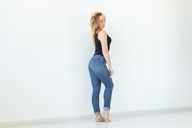 Young woman in jeans and black shirt standing over the white wall with copy space