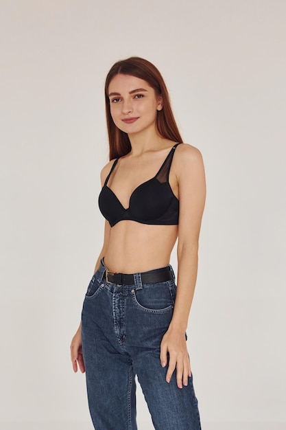 Young woman in jeans and bra indoors White background