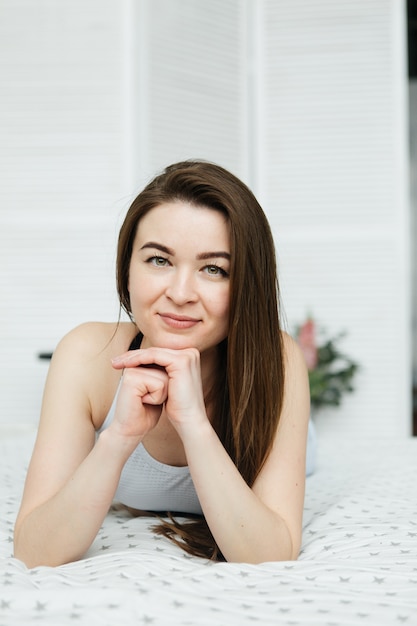 Young woman in jeans lying on the bed. Girl in light bedroom.