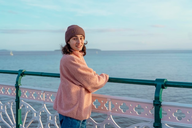 A young woman in jeans and a pink jacket resting on the seashore at sunset