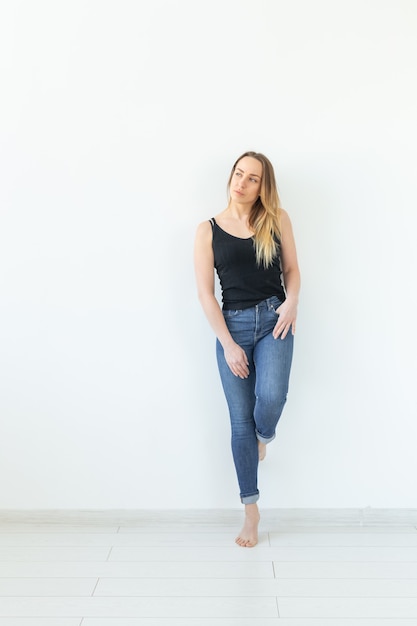 Молодая женщина в джинсах стоит над белой стеной и выглядит сексуально