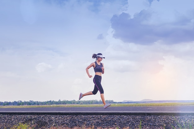 Young woman jogging along the road. with cloudy sky as background