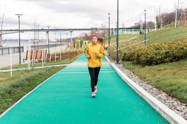 Young woman jogging in autumn park along the embankment