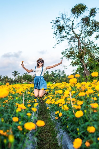 畑で花をかせている植物の真ん中にジャンプする若い女性