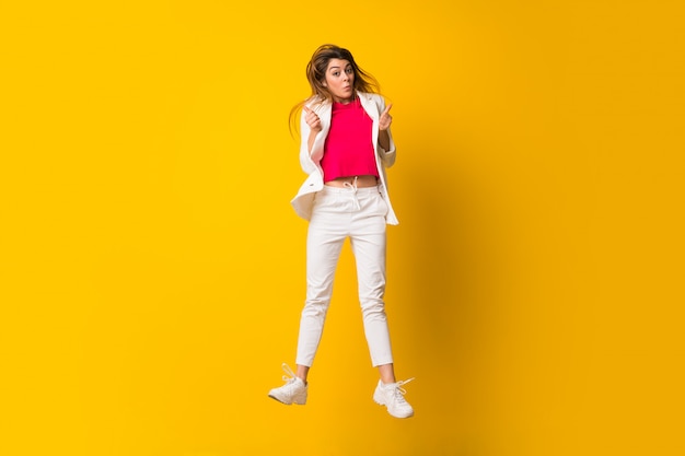 Young woman jumping over isolated yellow wall making victory gesture