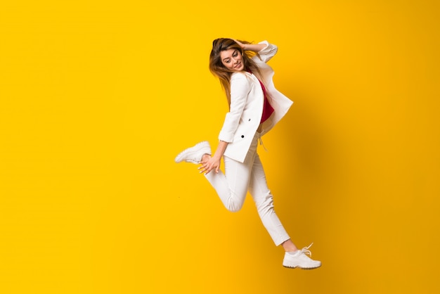 Young woman jumping over isolated yellow wall