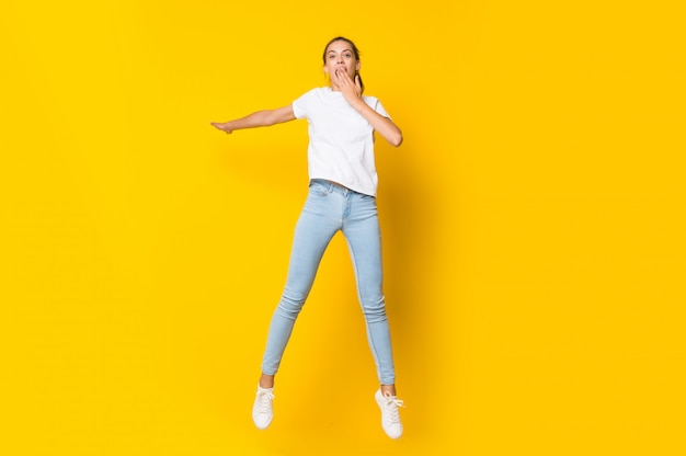 고립 된 노란색 벽 위로 점프하는 젊은 여자