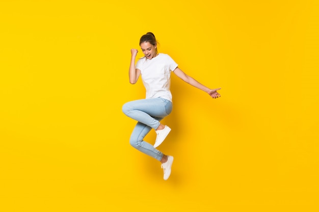 Young woman jumping over isolated yellow wall