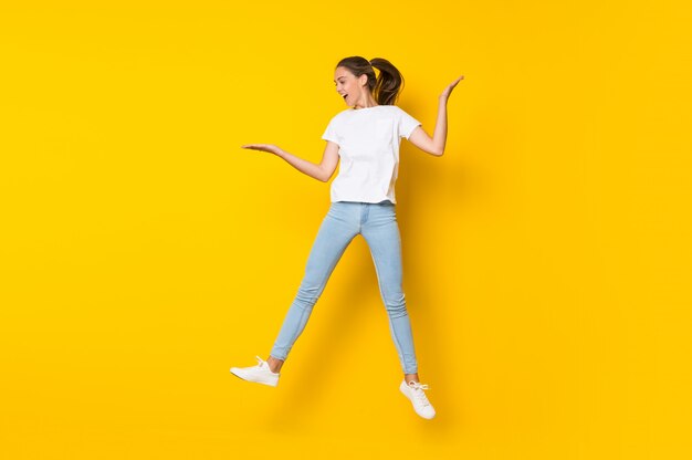 Young woman jumping over isolated yellow wall