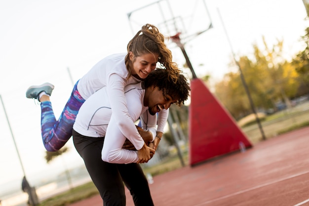 Young woman jumping on the men shoulders at outdoor basketball court