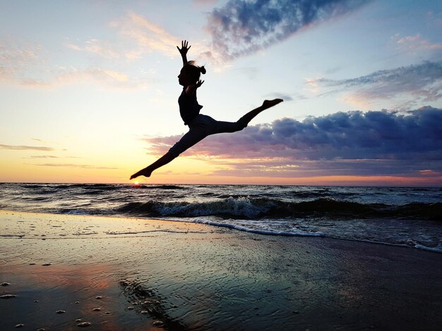 写真 夕暮れの空に向かってビーチで海岸にジャンプする若い女性