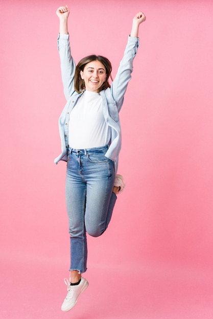 Young woman jumping on pink wall