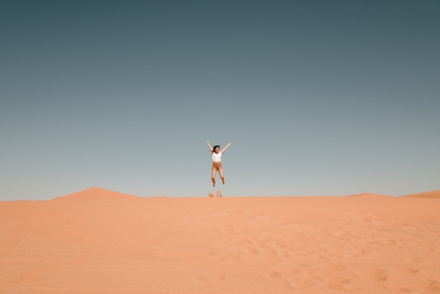 Young woman jumping over a sand dune in the desert