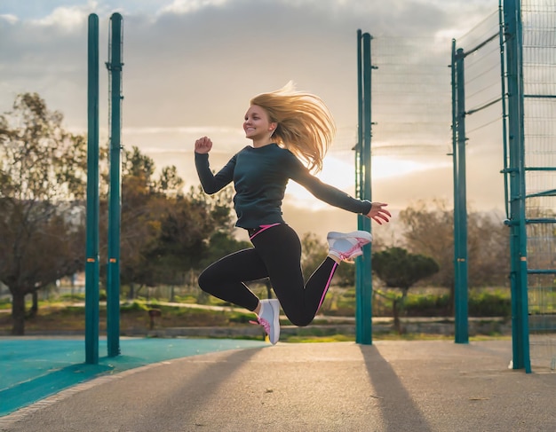 Photo young woman jumping in sports park at sunset