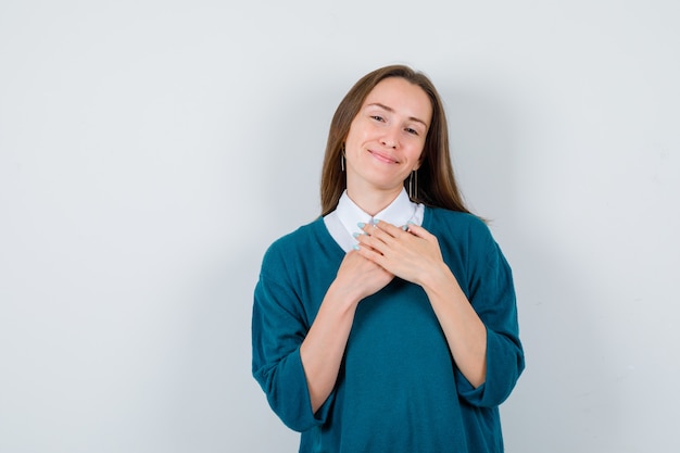 Photo young woman keeping hands on chest in sweater over white shirt and looking delighted. front view.