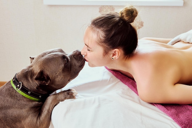 Фото Молодая женщина целует свою собаку, лежа на массажном столе в массажном салоне
