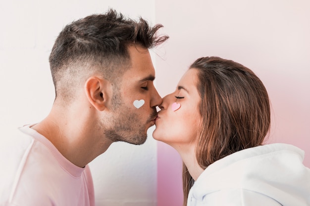 Photo young woman kissing man with paper hearts on faces