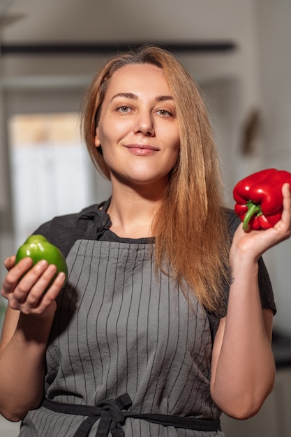 Young woman in the kitchen in an apron with red sweet and green peppers in her hands