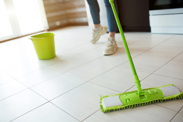 Young woman on kitchen. Cleaning floor with green mop. Low cut view. Making floor more clean. Green bucket with water behind.