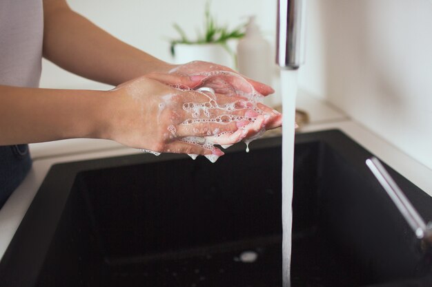 Giovane donna in cucina durante la quarantena. tagli la vista delle mani del caucasico nelle bolle di sapone bianche tengono la spugna. lavarsi le mani.