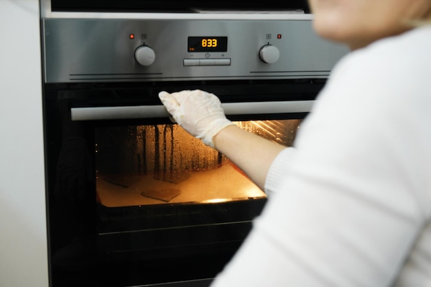 Young woman in the kitchen is cooking food in the oven The light from the oven checks the readiness of pastries