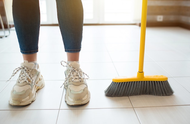 Photo young woman in kitchen. stand alone after sweeping floor. hold broom with hand. householding on free time.