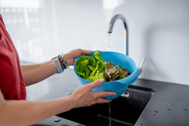 Young woman in kitchen washes lettuce leaves in closeup view
