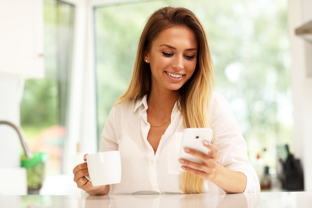 Giovane donna in cucina con smartphone