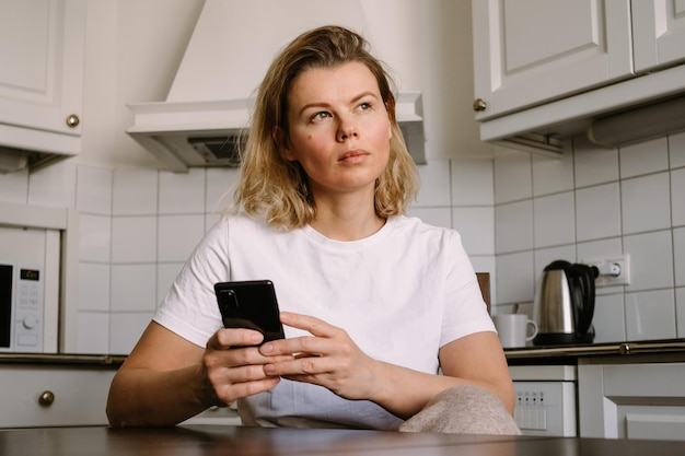 Молодая женщина на кухне работает со смартфоном