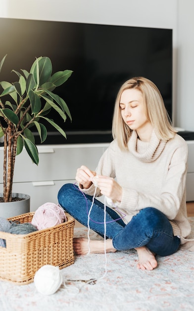 Young woman knitting warm scarf indoors