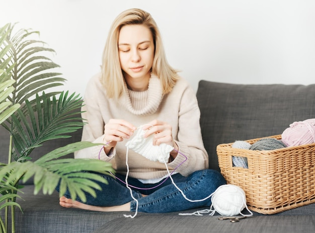 Young woman knitting warm scarf indoors