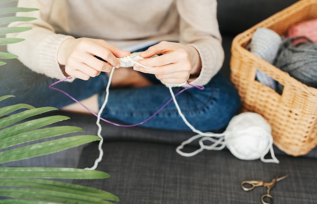 Young woman knitting warm scarf indoors