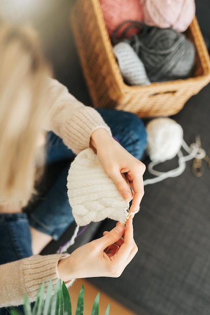 Young woman knitting warm scarf indoors