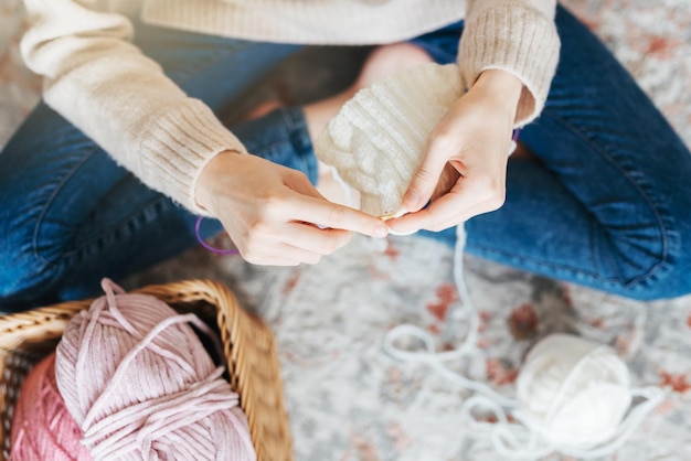 Young woman knitting warm scarf indoors