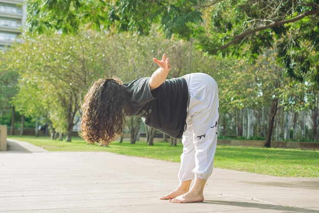 Young woman latina dancer warms up in a city park stretches legs copy space