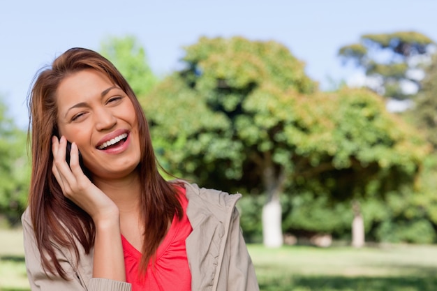 明るい公園のエリアで電話で喜んで笑っている若い女性