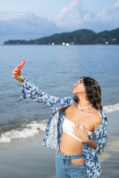 ビーチで携帯電話で Selfie を取りながら笑っている若い女性