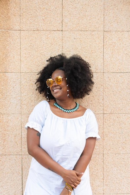 A young woman laughs against a wall She wears sunglasses and afro hair