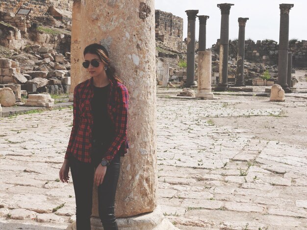 Foto giovane donna appoggiata a una colonna presso vecchie rovine storiche