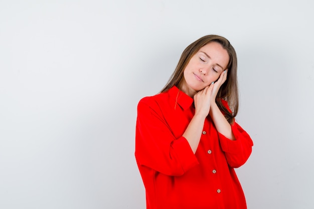 Young woman leaning on palms as pillow in red blouse and looking peaceful , front view.